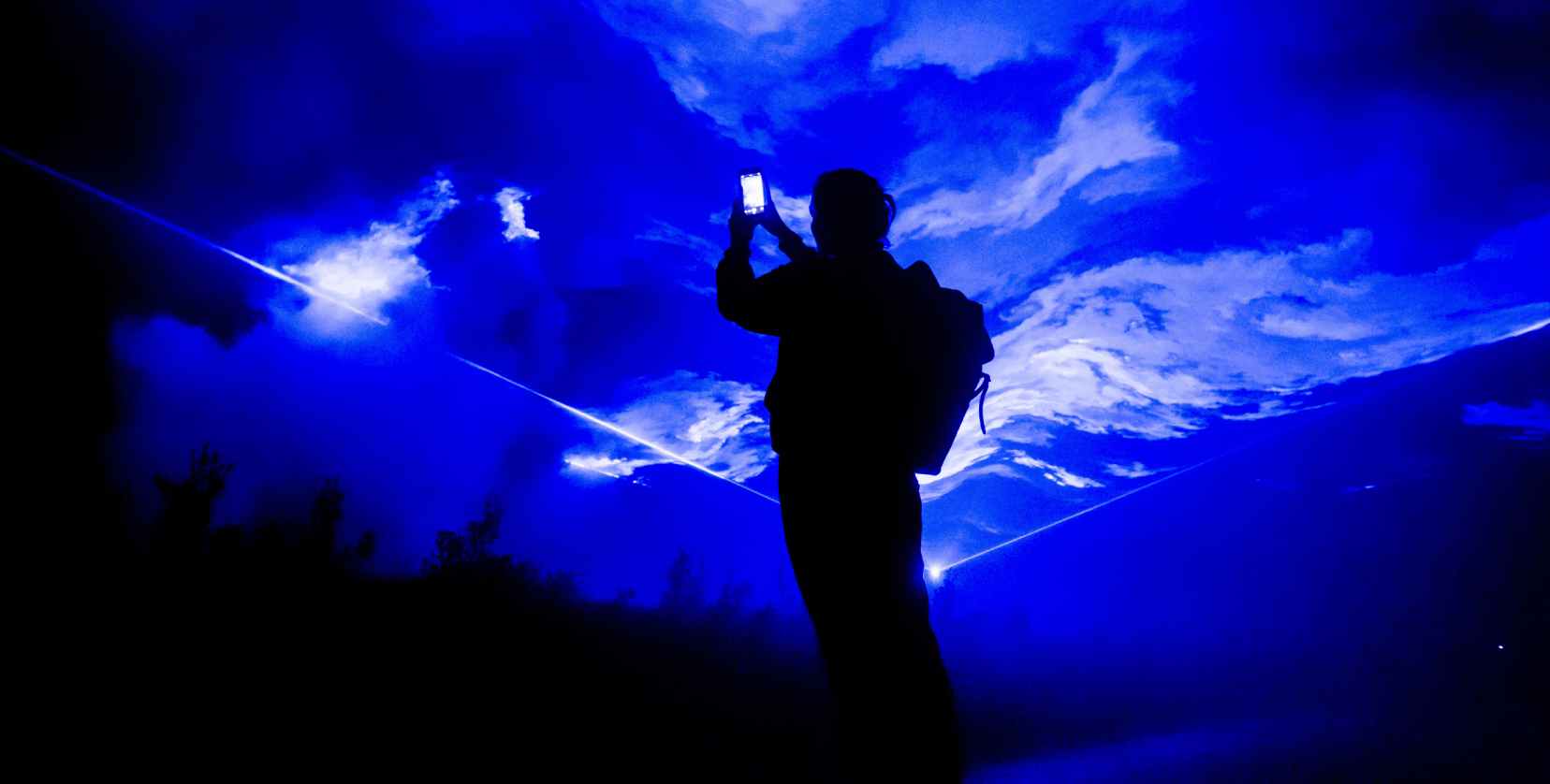 A figure stands silhouetted against a projection of bright blue and white swirling clouds.